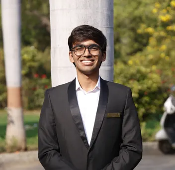 Maitreya Sapariya standing outdoors in a black blazer and glasses, smiling